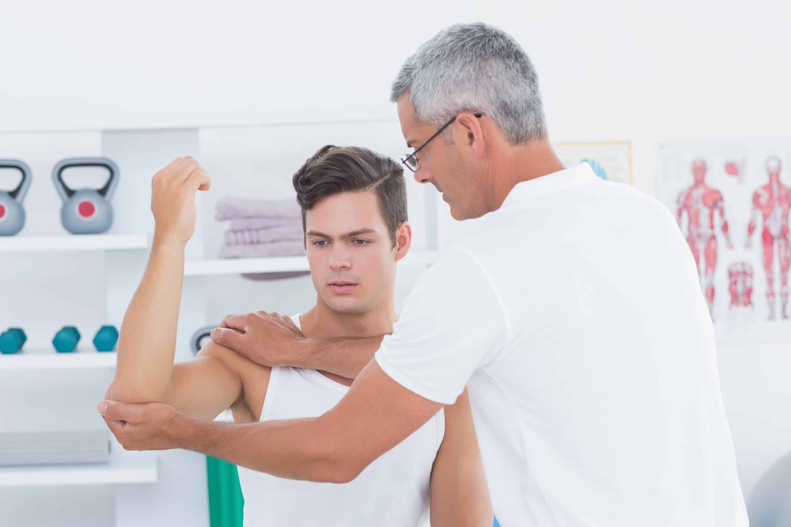 Doctor stretching a young man arm in medical office